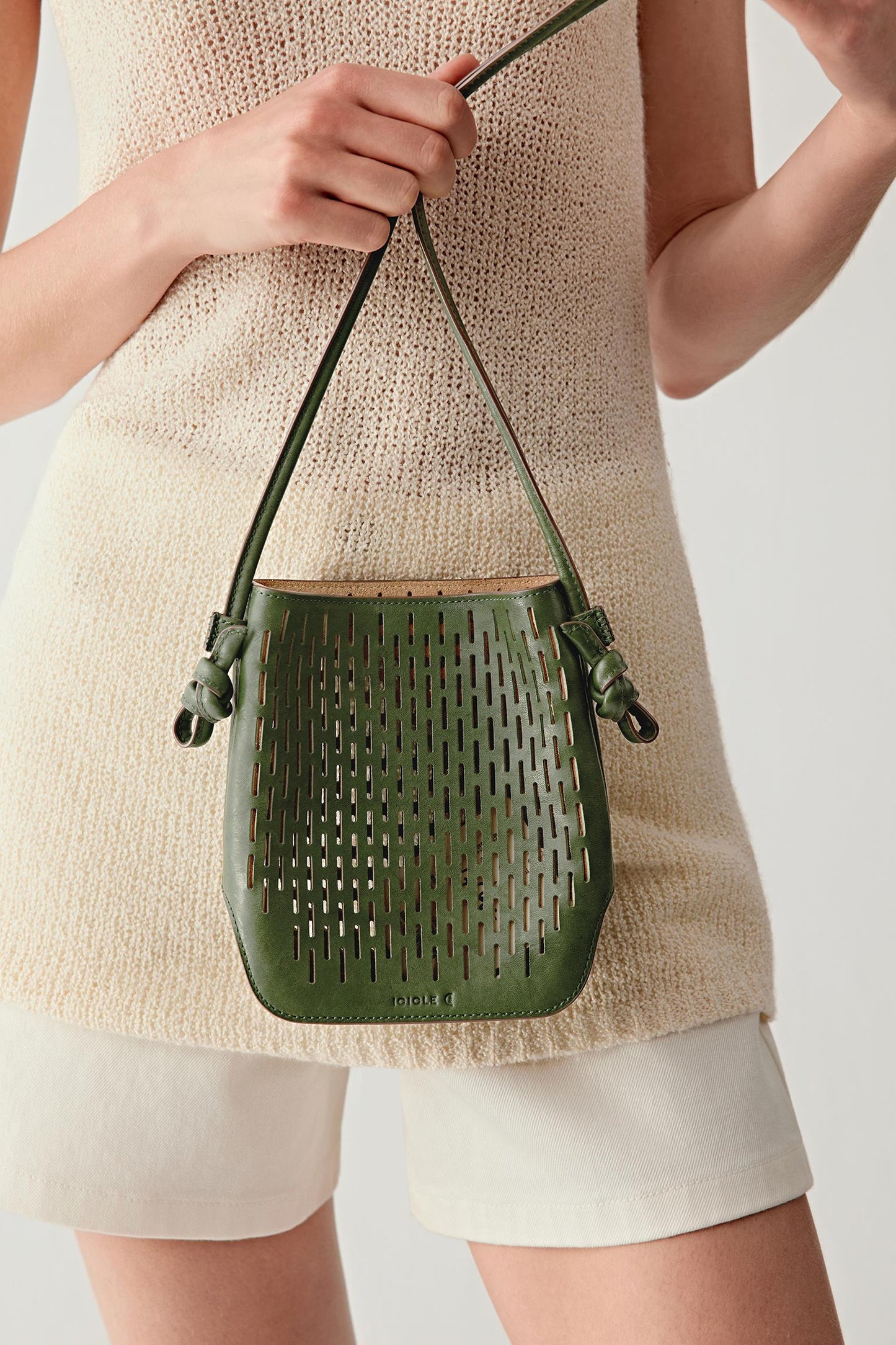 Side detail showing the khaki green leather crossbody bag at hip level, emphasizing the knotted strap detail and flexible perforated leather.