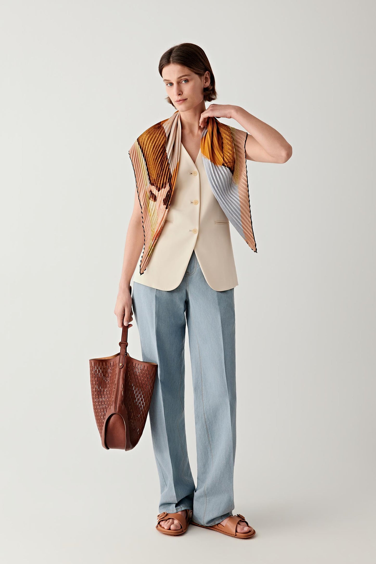 Woman wearing an ochre silk twill scarf draped over a light outfit, front view.