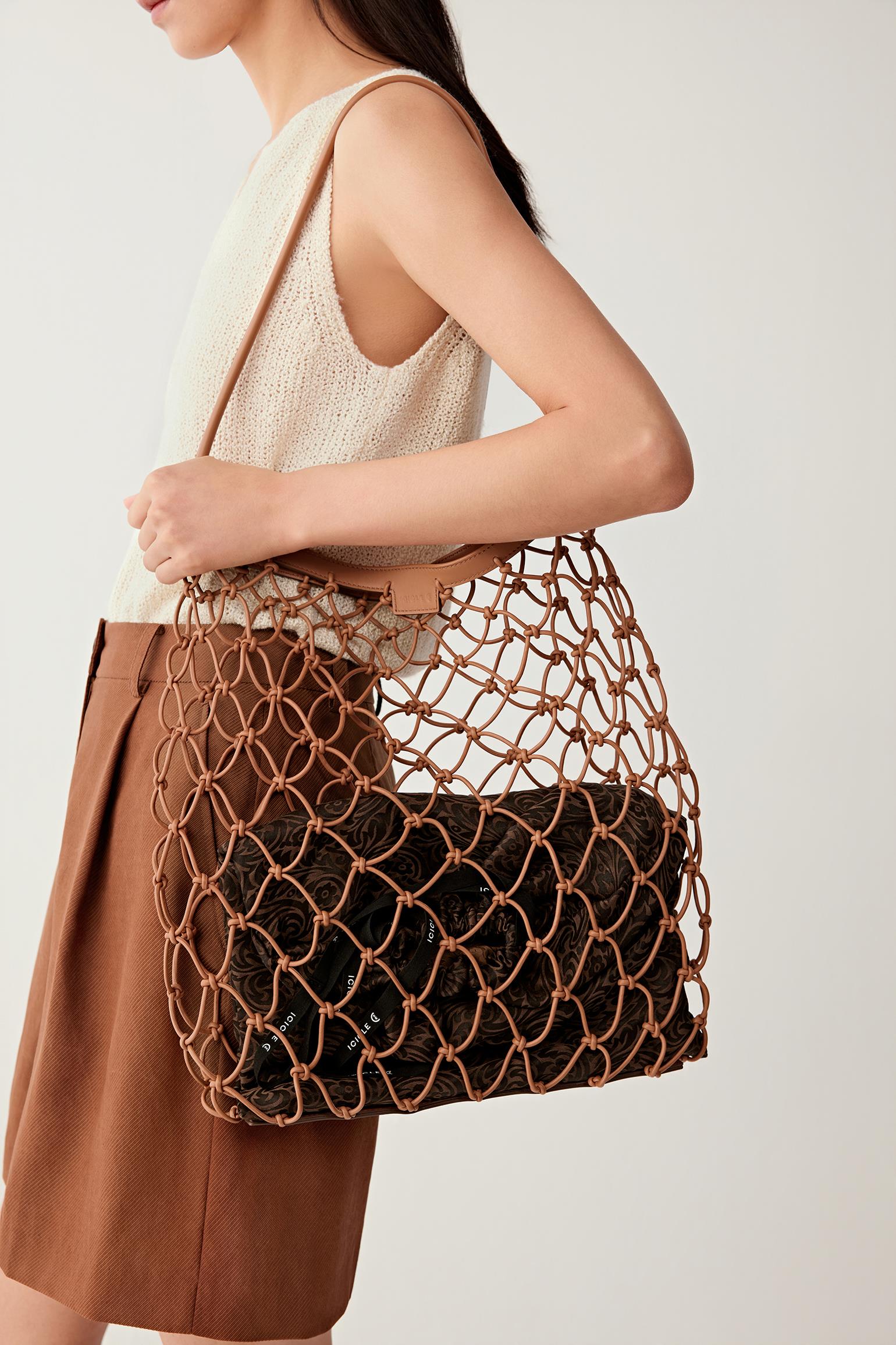 Woman wearing a camel nappa leather net bag with an open mesh structure and leather trim, carried on the shoulder, close side view highlighting the contrast between the structured inner pouch and flexible net.