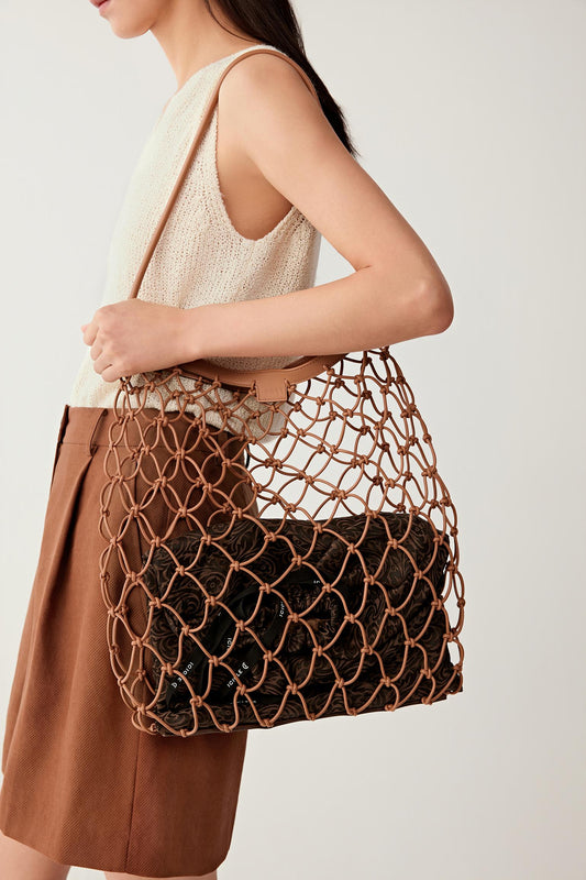 Woman wearing a camel nappa leather net bag with an open mesh structure and leather trim, carried on the shoulder, close side view highlighting the contrast between the structured inner pouch and flexible net.