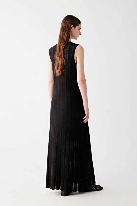 Full-length side view of the dress, highlighting the vertical fall from shoulder to hem, the way the knit fabric follows the body with a light, flexible structure and the gradual flare toward the bottom