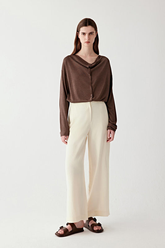 Full-length front view of a woman standing facing forward wearing a dark brown tussah silk draped cardigan, paired with light ivory wide-leg trousers, highlighting the fluid silhouette, dropped shoulders and softly draped neckline, with a naturally textured, matte surface characteristic of tussah silk yarn