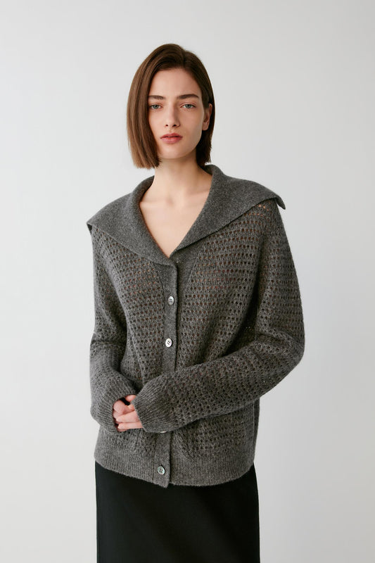 A woman wearing a textured gray knit cardigan with a wide collar and button front, paired with a black skirt, photographed against a plain light gray studio background.