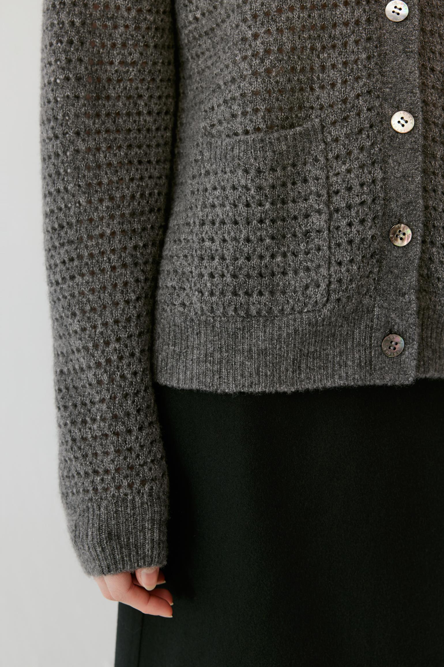 Close-up of a person wearing a textured gray knit cardigan with silver buttons and a dark skirt against a light gray background.
