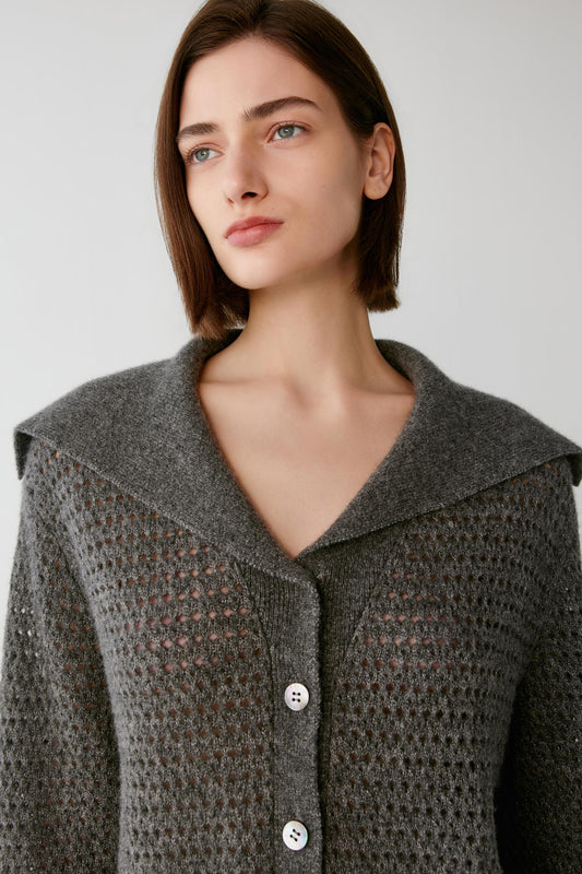 A woman wearing a textured gray knit cardigan with a wide collar and three white buttons, photographed against a plain light gray background.