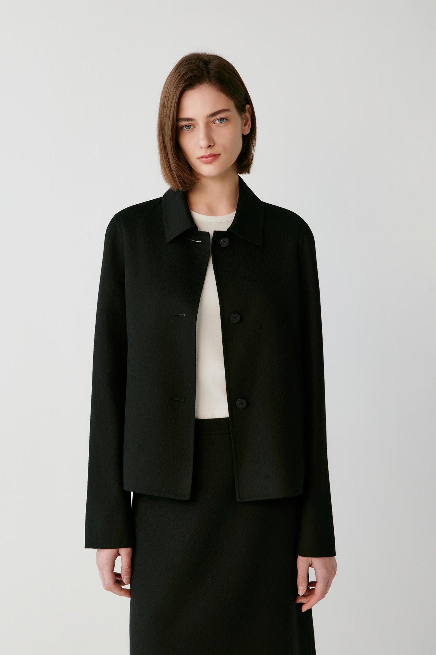 Woman wearing a short black button-up jacket over a white top and black skirt.