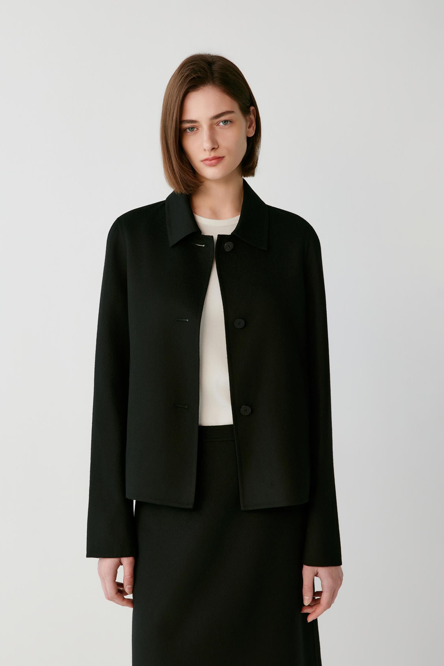 Woman wearing a short black button-up jacket over a white top and black skirt.