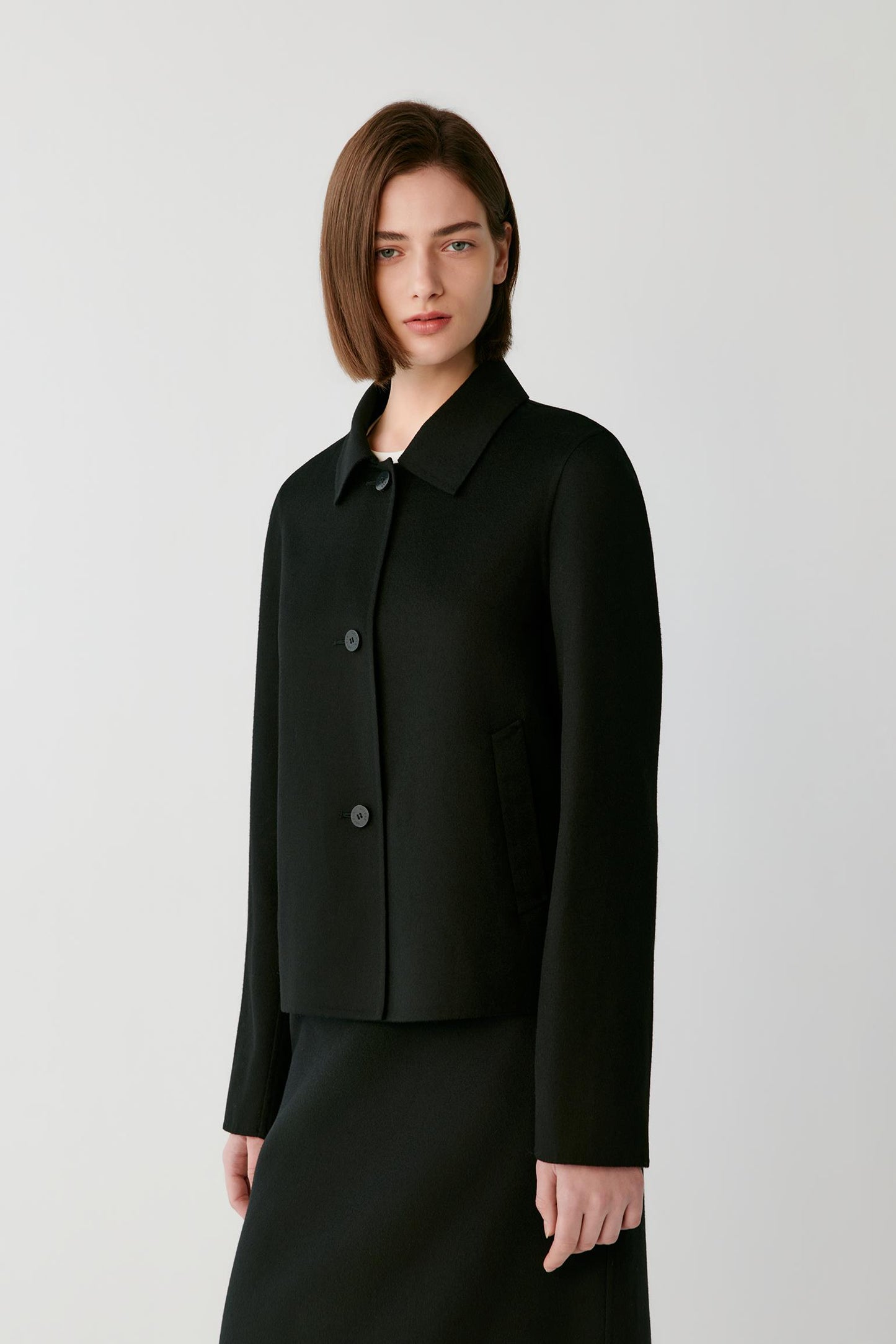 Woman wearing a short black button jacket over a white top and black skirt.