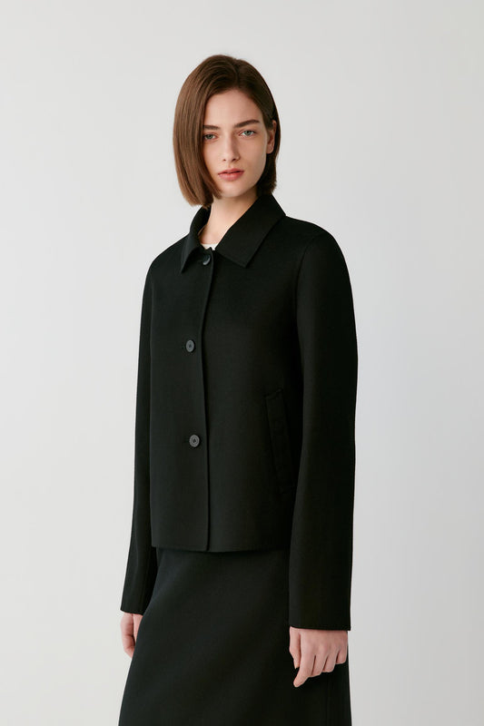 Woman wearing a short black button jacket over a white top and black skirt.