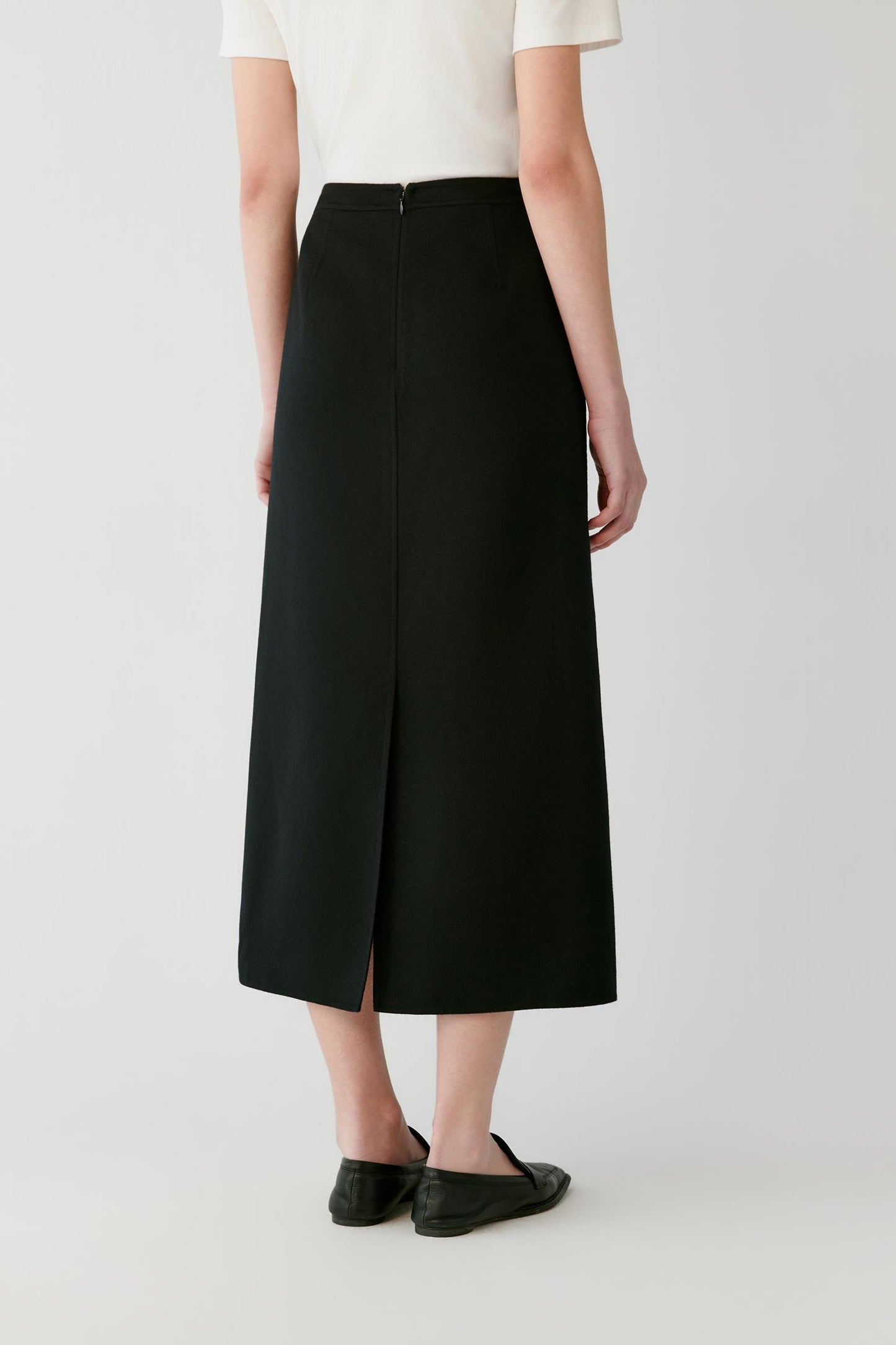 Back view of a woman wearing a black A-line midi skirt with a centre slit.
