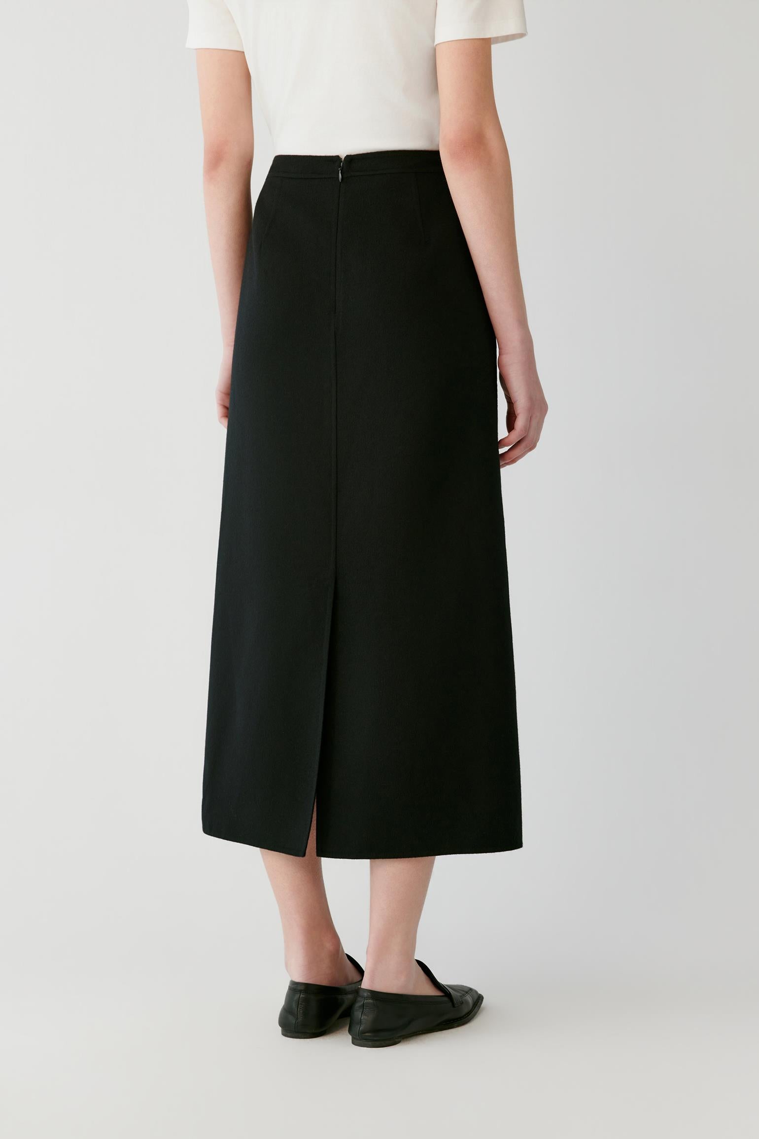Back view of a woman wearing a black A-line midi skirt with a centre slit.