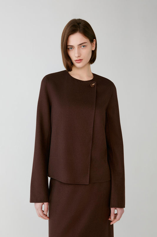 A woman modeling a dark brown wrap-style jacket with a single decorative button detail at the collar, paired with a matching brown skirt, against a light gray studio background.