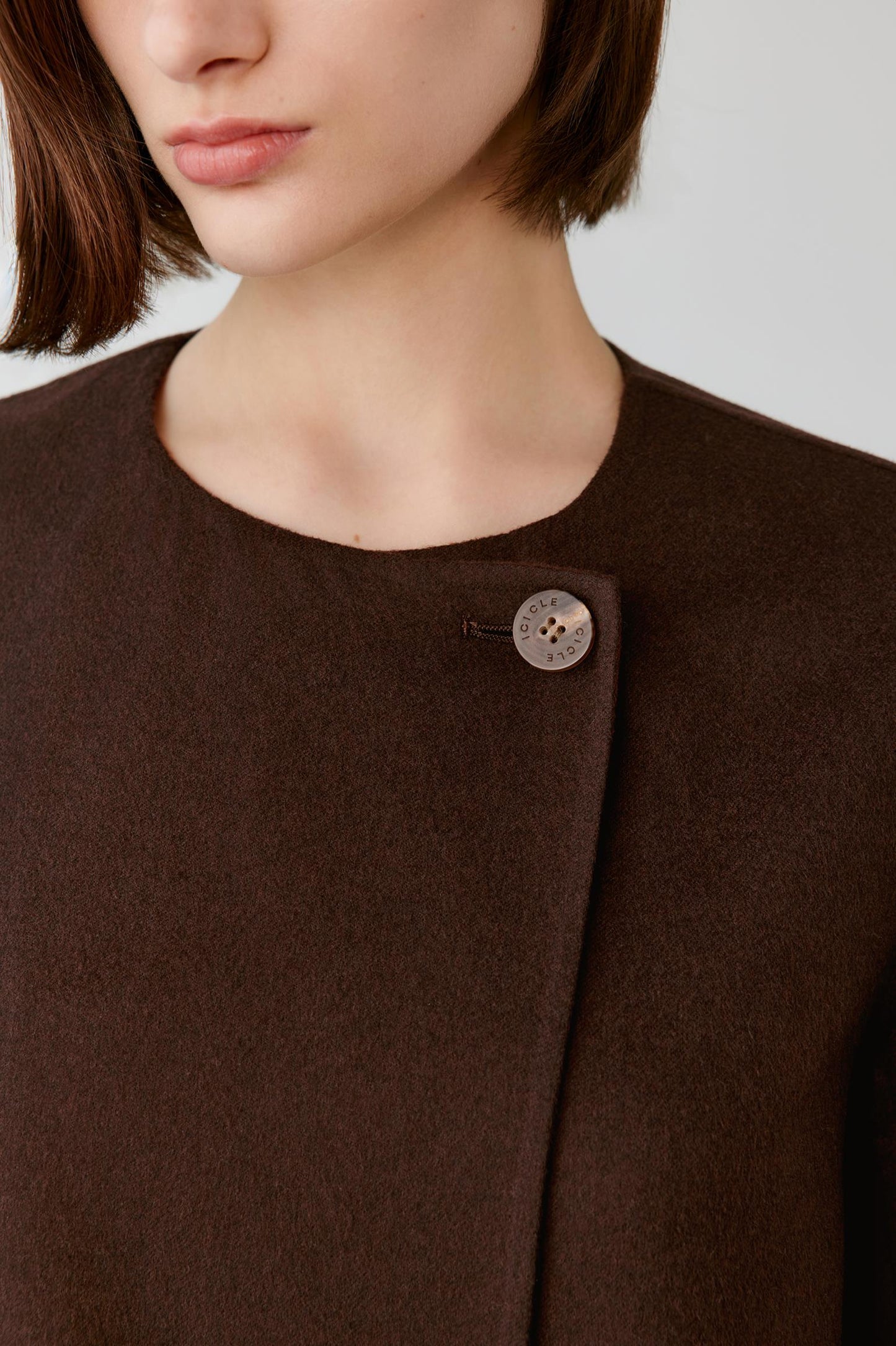 Close-up of a model wearing a dark brown wool coat with a single decorative button detail on the shoulder.