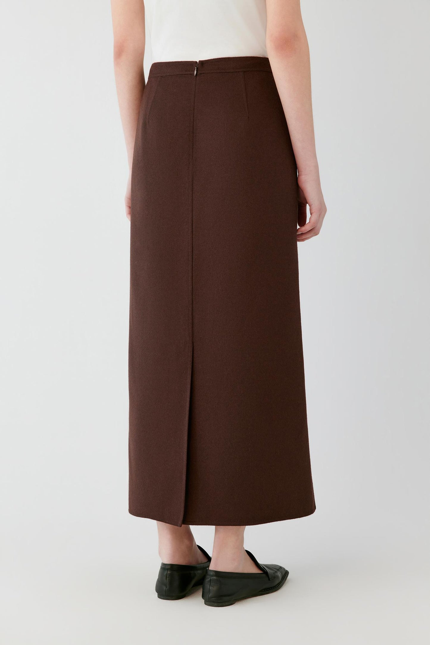 Back view of a woman wearing a brown A-line midi skirt with a centre slit.