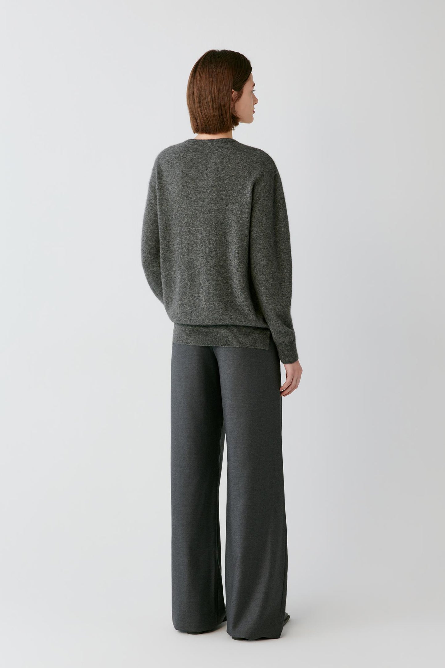 A woman shown from the back wearing a dark gray knit sweater and matching wide-leg trousers against a light gray studio background.