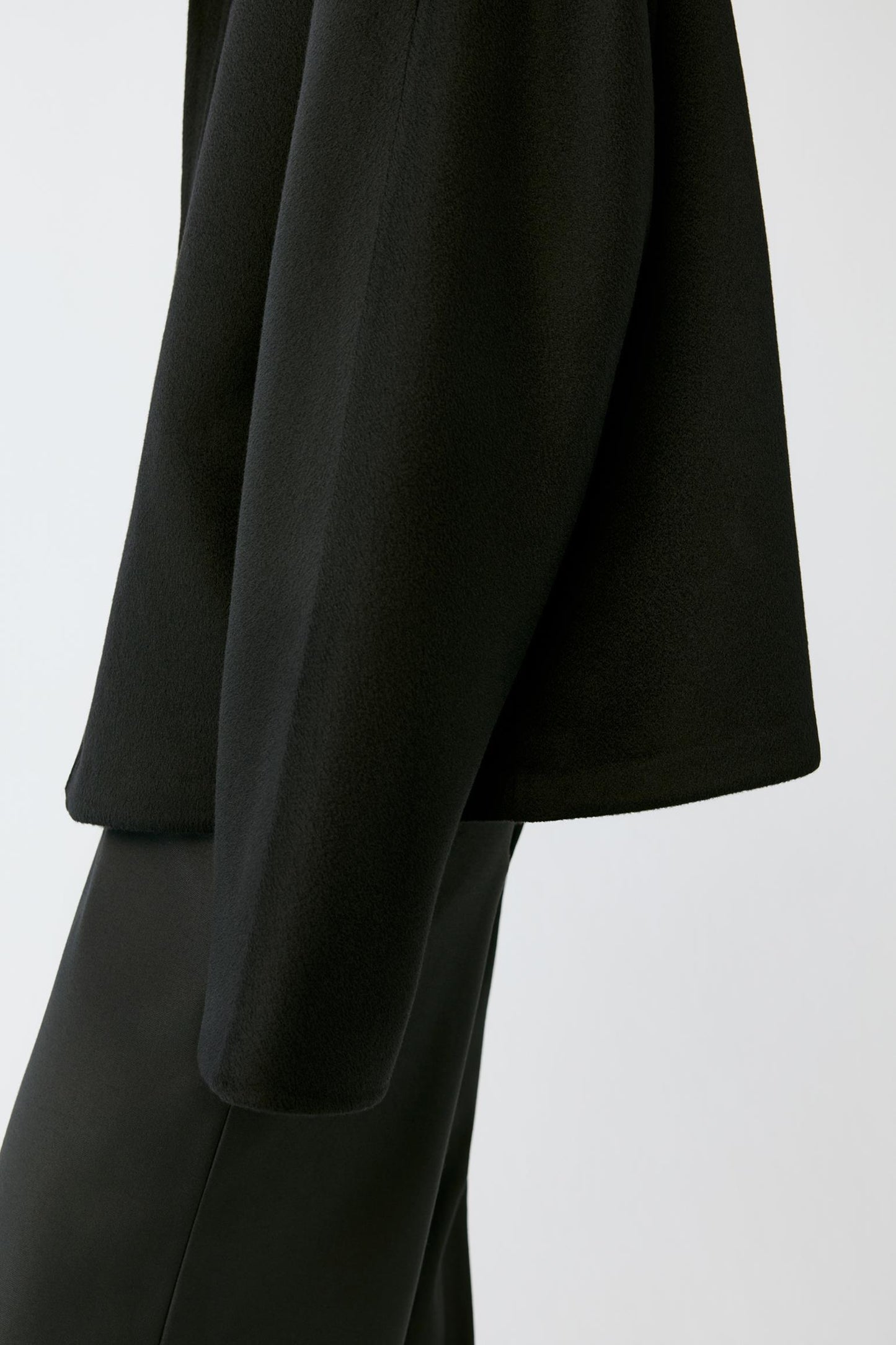 A model wearing a black zip-up jacket with a high mock neck collar, photographed against a neutral light gray background.
