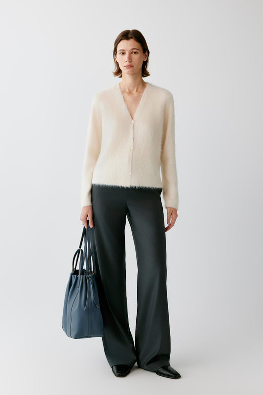 Woman wearing a cream fuzzy cardigan and dark wide-leg trousers, carrying a blue tote bag.