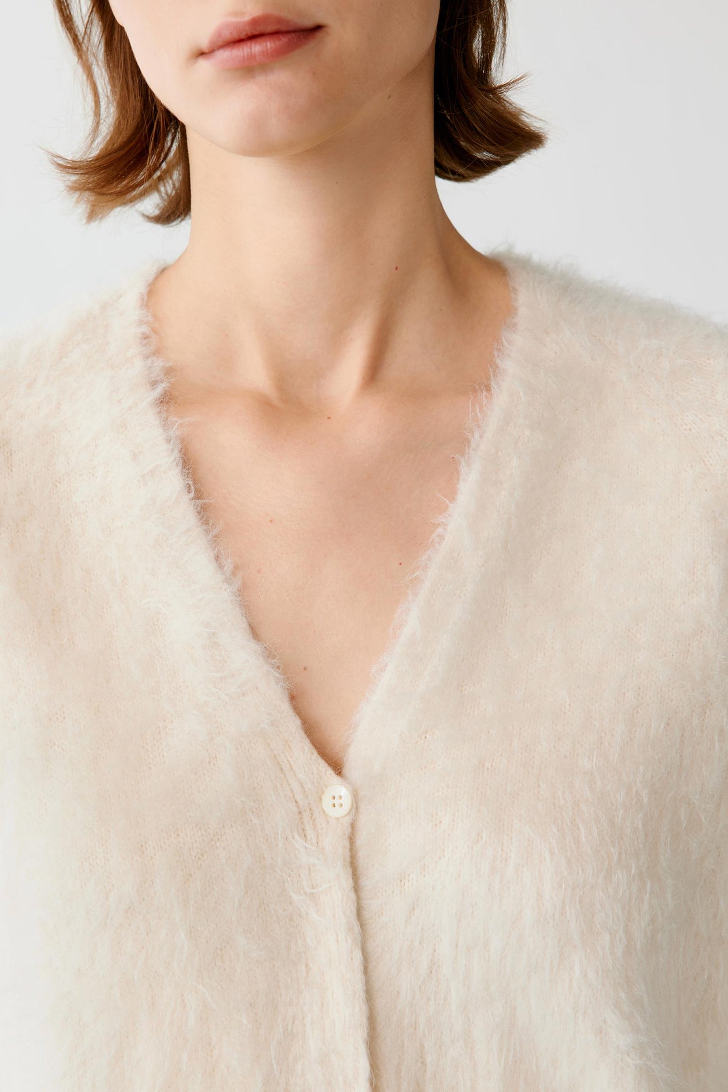 Close-up of the V-neckline and soft fuzzy texture of a cream button-up cardigan.