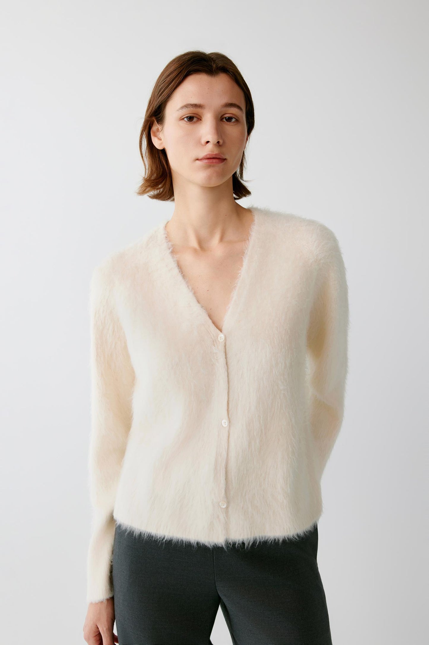 Woman wearing a cream fuzzy V-neck button-up cardigan.