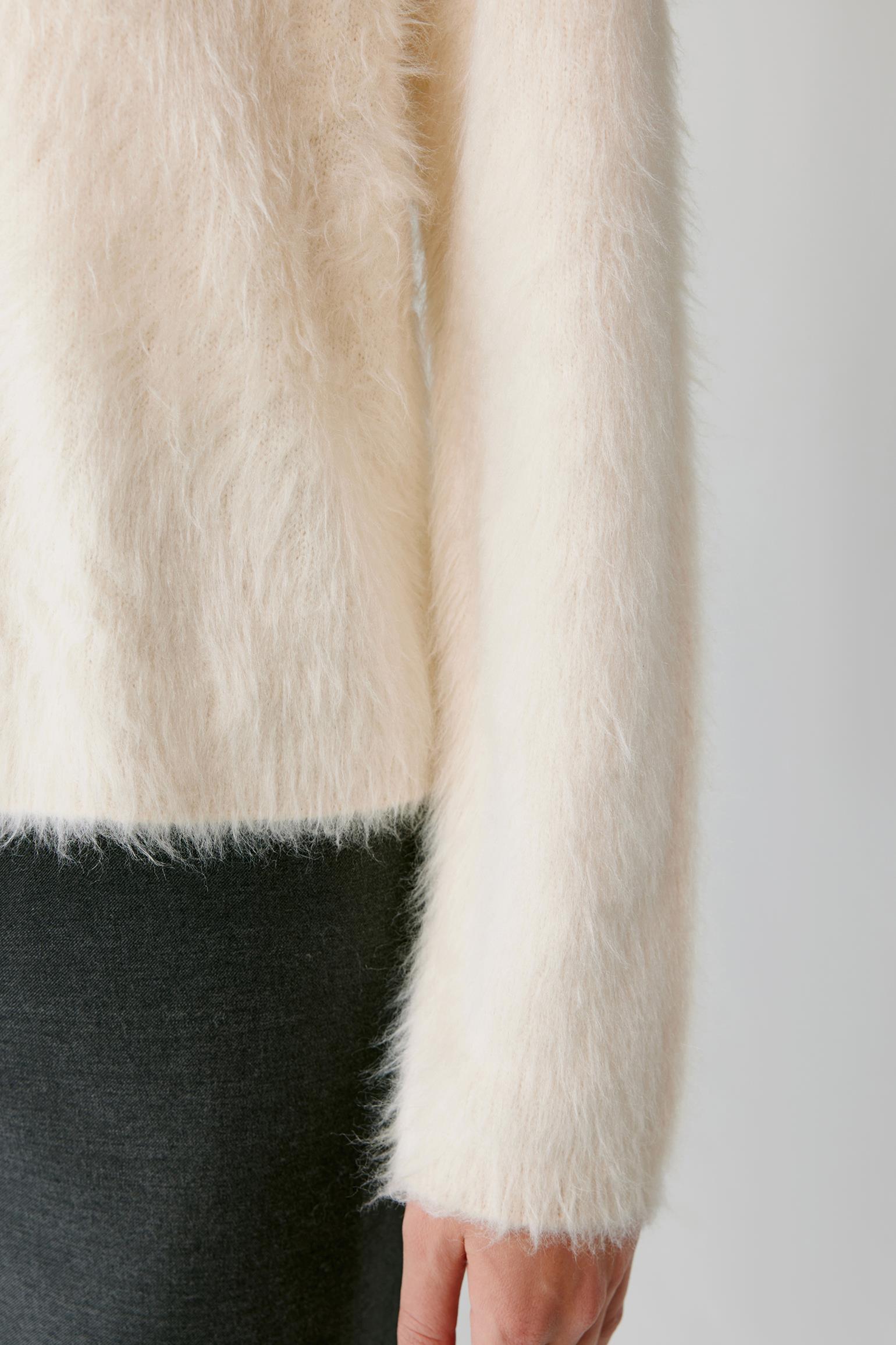 Close-up of the hem and long sleeve of a cream fuzzy cardigan.