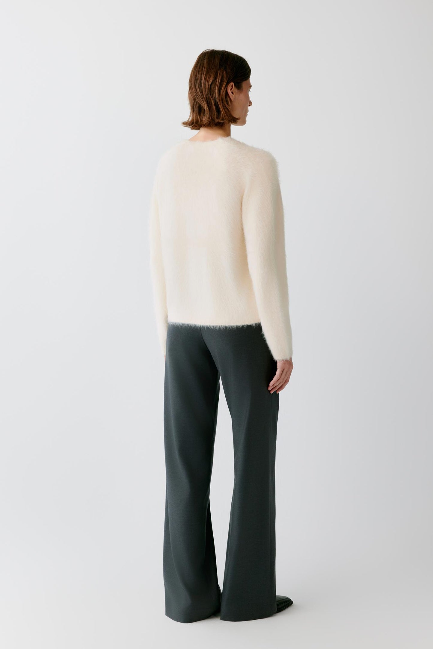 Back view of a woman wearing a cream fuzzy cardigan and dark wide-leg trousers.