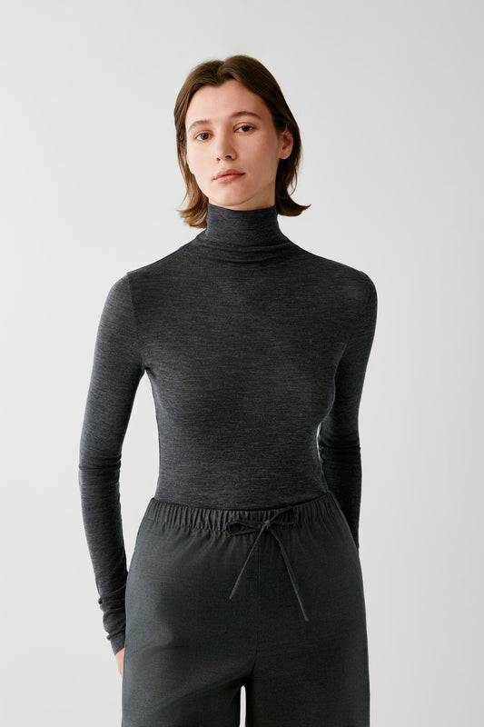 A woman modeling a dark charcoal gray long-sleeve turtleneck top with matching dark drawstring sweatpants against a light gray studio background.