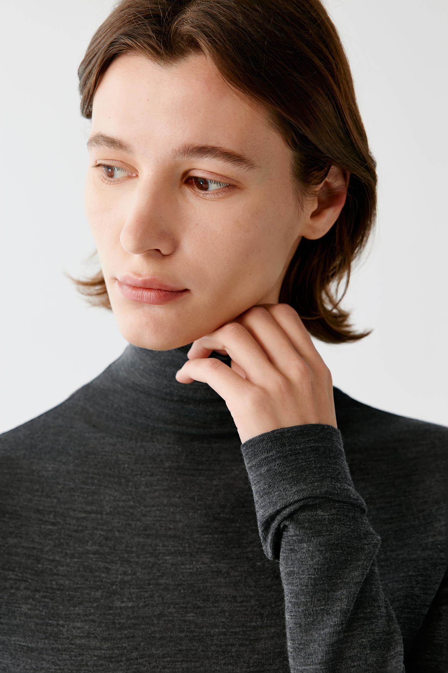 A close-up of a person wearing a dark charcoal gray ribbed turtleneck sweater against a light gray background.
