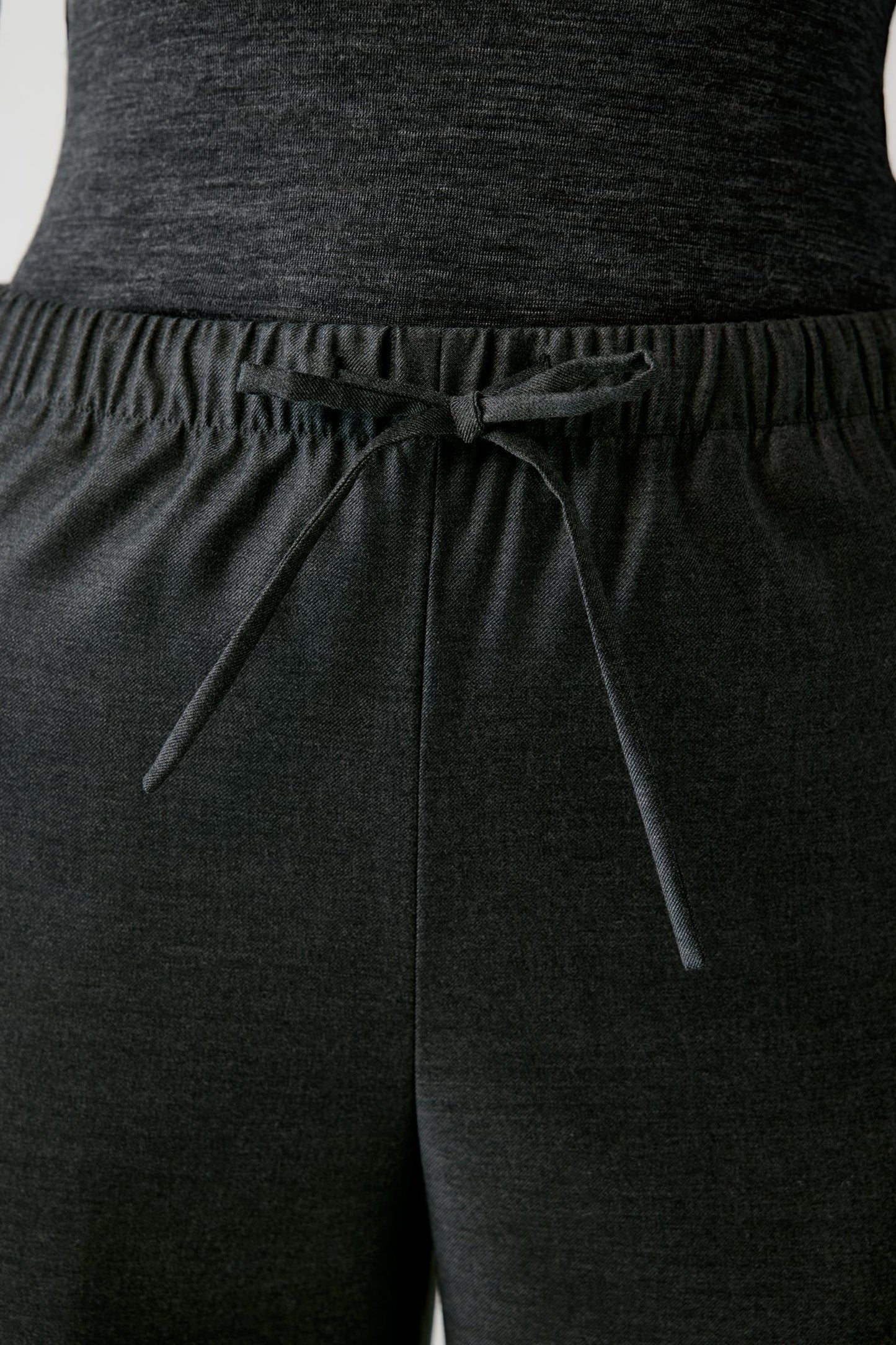 Close-up of dark charcoal gray heathered lounge pants with an elastic drawstring waistband, worn with a matching dark top.