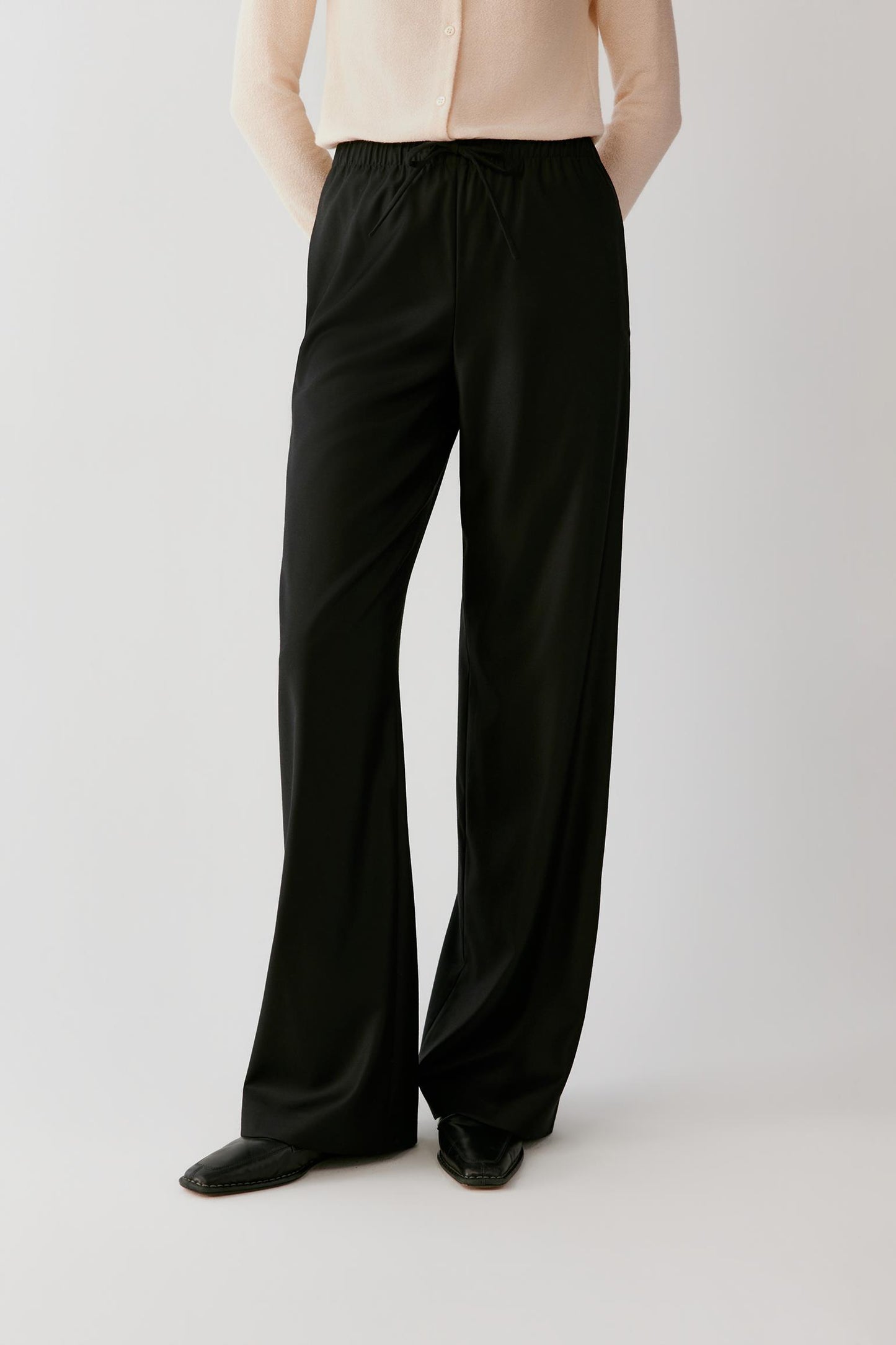 Woman wearing fluid black wide-leg trousers with an elasticated waistband.