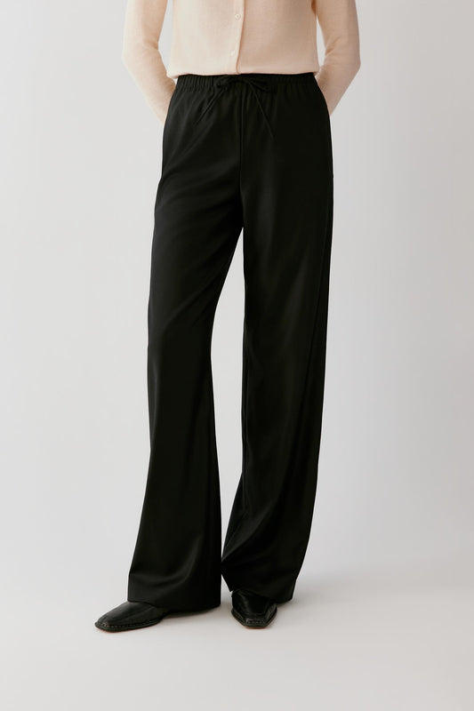 Woman wearing fluid black wide-leg trousers with an elasticated waistband.