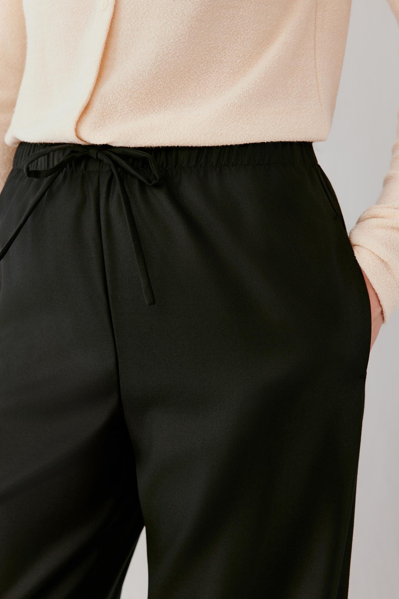 Woman wearing fluid black wide-leg trousers with an elasticated waistband.