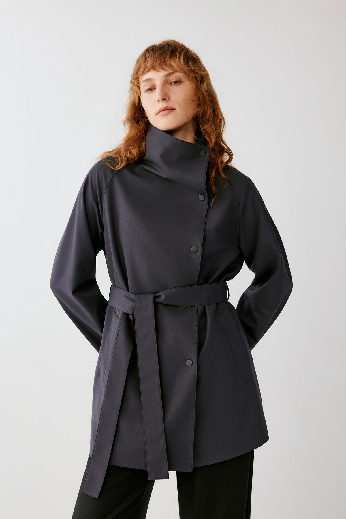 Three-quarter front view emphasizing the self-fabric belt, concealed fastening and fluid drape of the dense wool fabric.