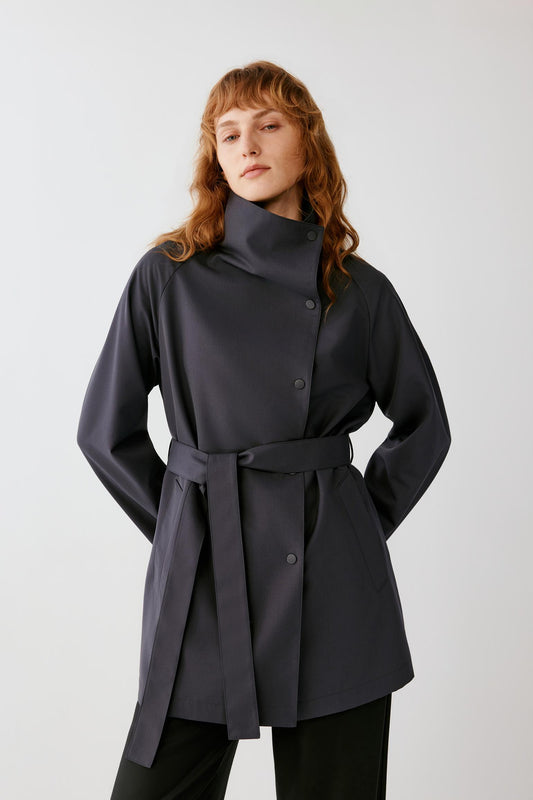 Three-quarter front view emphasizing the self-fabric belt, concealed fastening and fluid drape of the dense wool fabric.