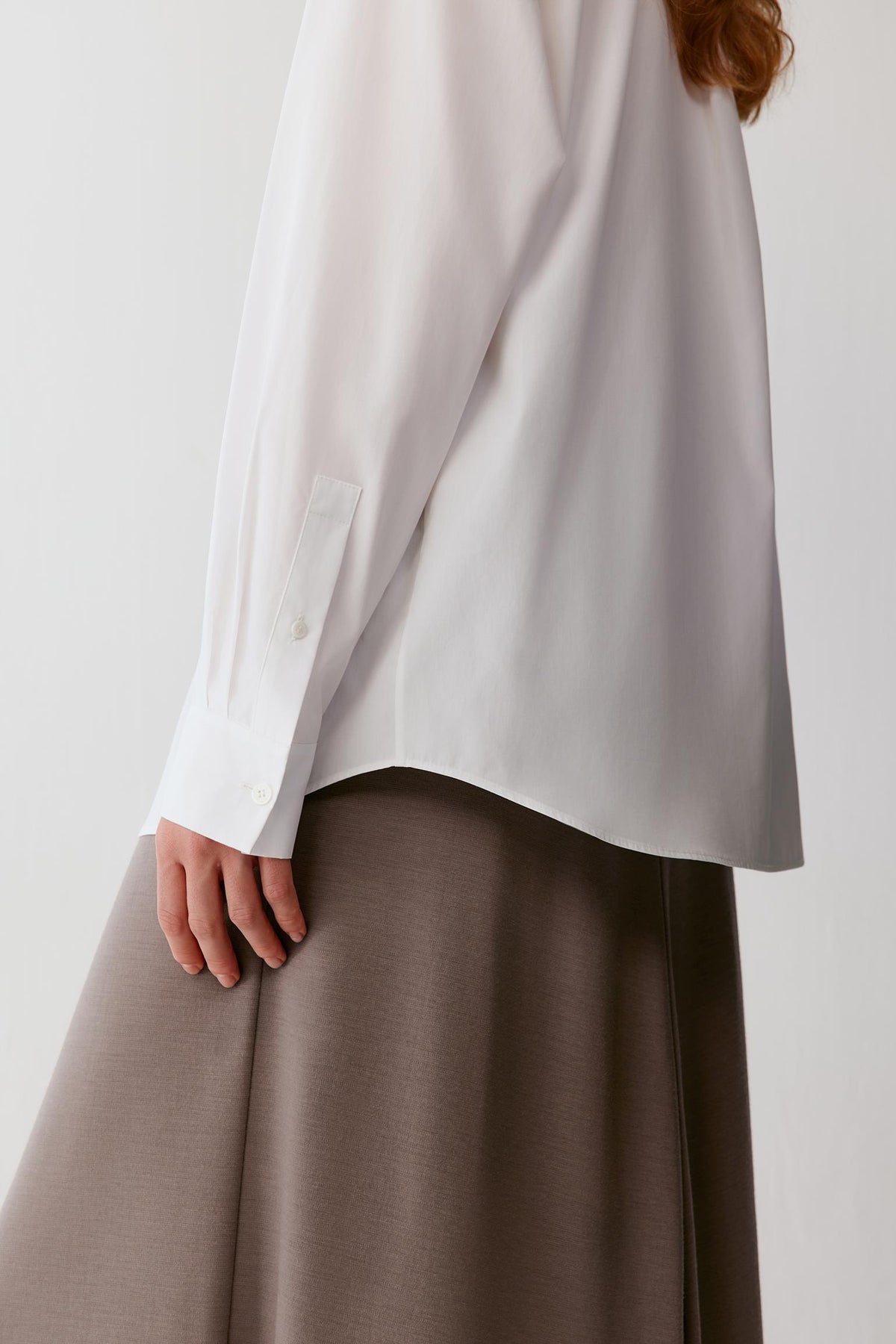 A close-up of a person wearing an oversized white long-sleeve blouse and a taupe brown skirt against a plain light background.