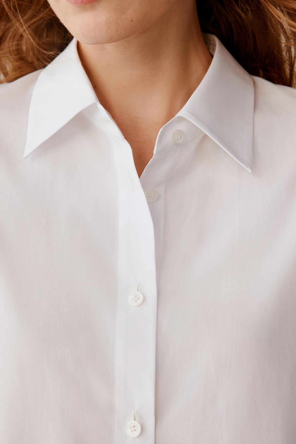 Close-up of a model wearing a white long-sleeve button-down shirt, showing the collar, front placket, and white buttons.
