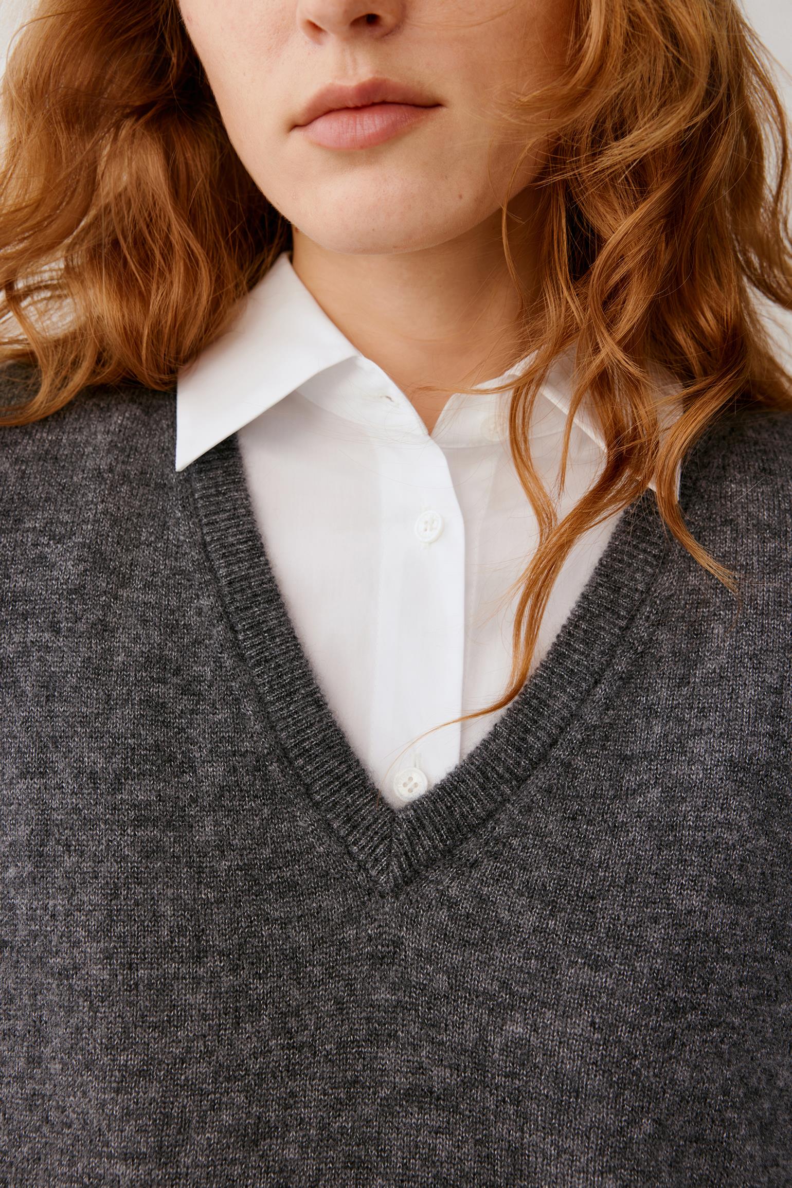 Close-up of a person wearing a dark gray V-neck knit sweater over a white collared button-up shirt.