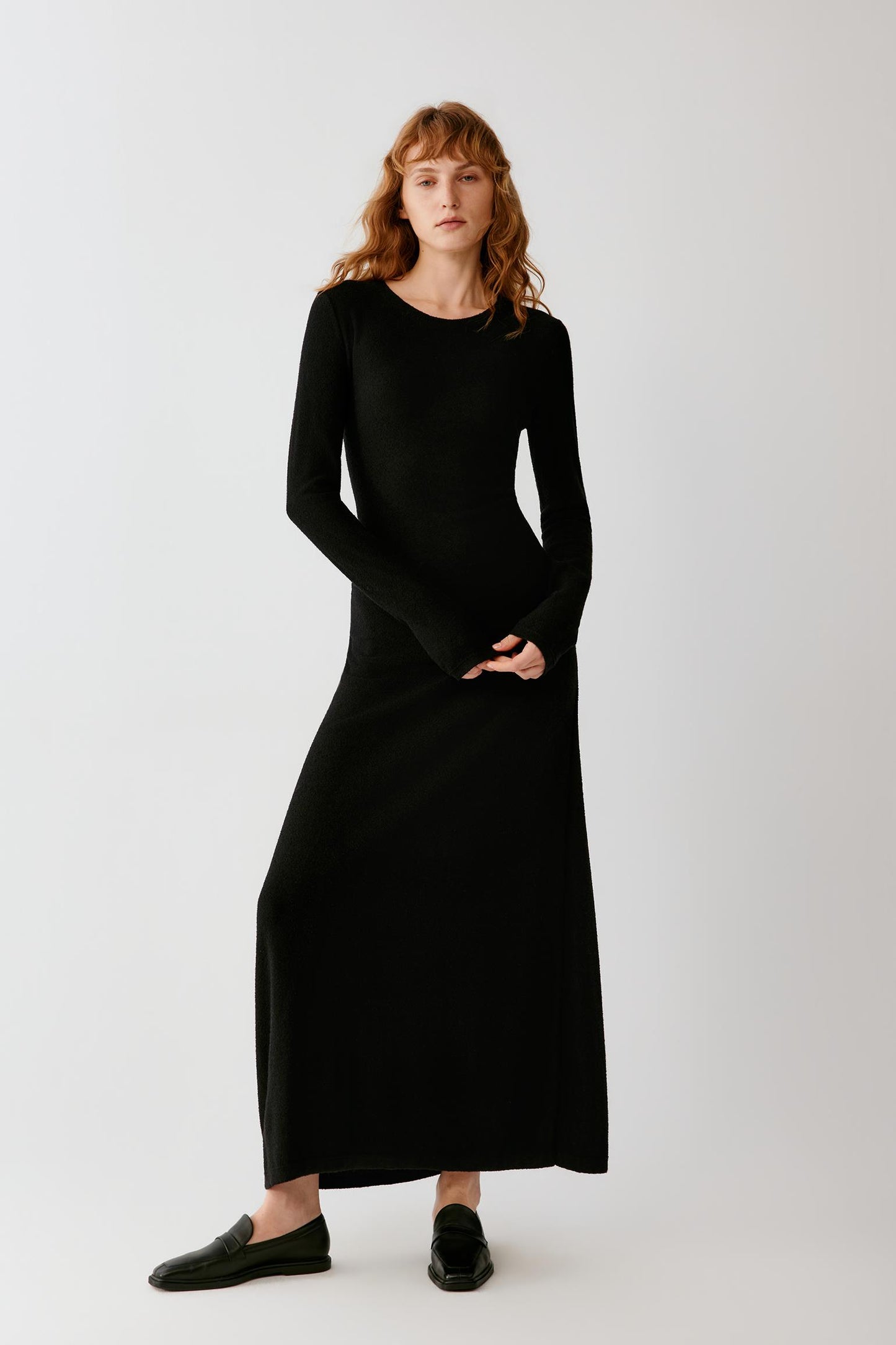 Woman wearing a long black fitted dress with long sleeves and black loafers.