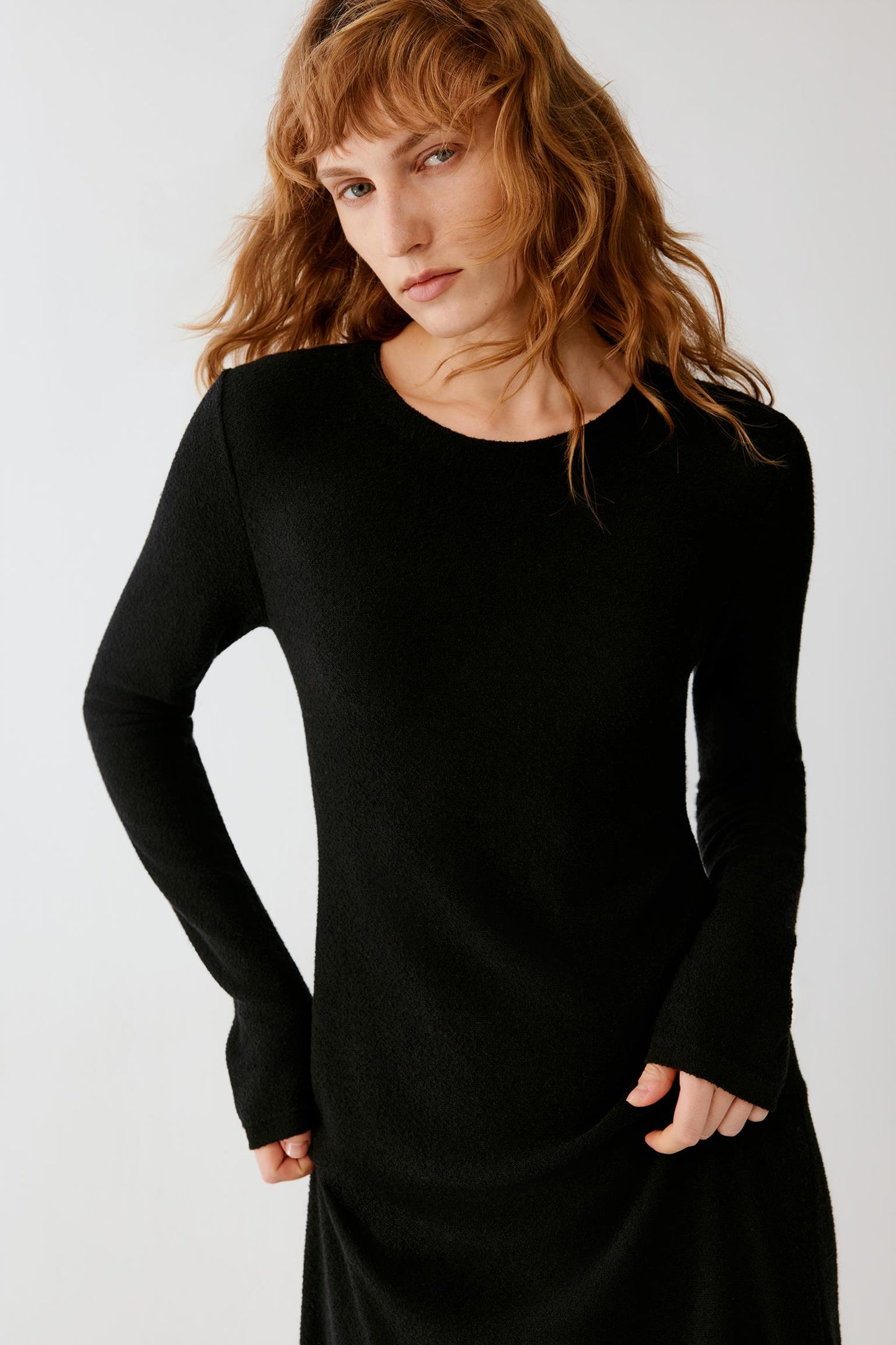 Woman wearing a long black fitted dress with long sleeves and black loafers.