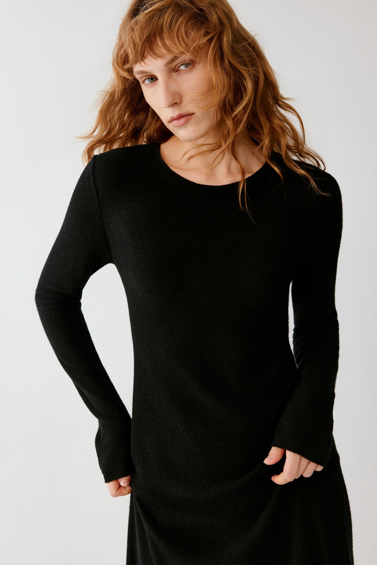 Woman wearing a long black fitted dress with long sleeves and black loafers.