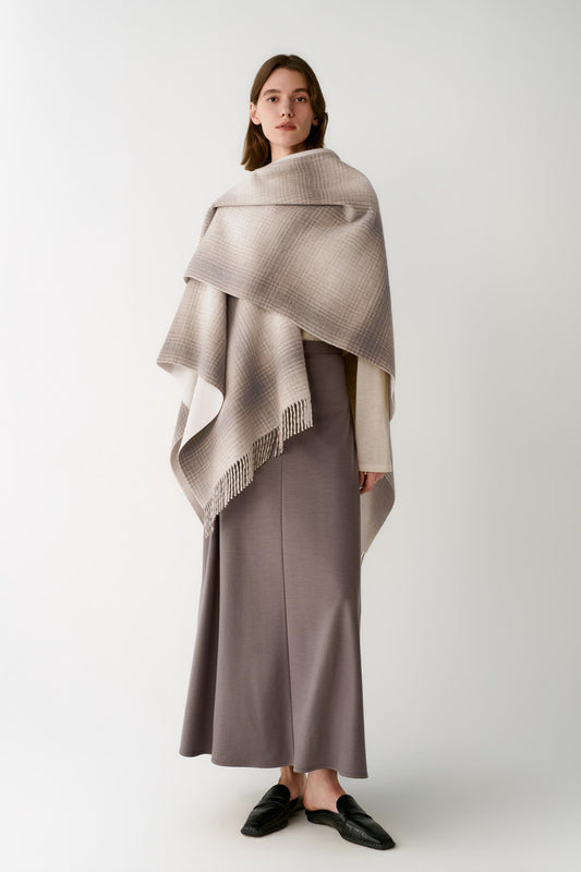 Front view of a woman wearing a beige ombré wool and cashmere shawl, showing the asymmetric drape and fringed trims.