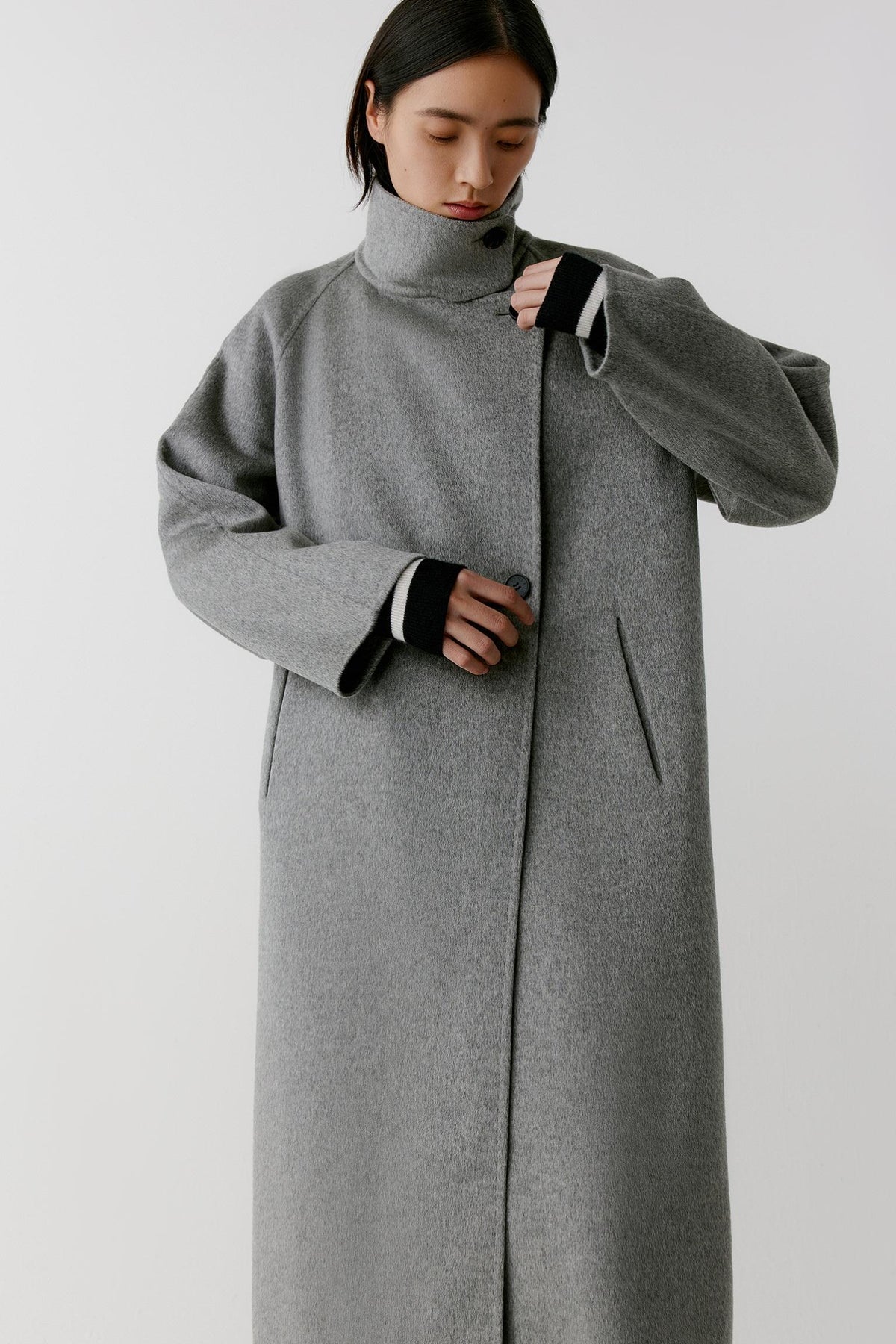Three-quarter view highlighting the long cut, raglan sleeves and structured drape of the grey melange double-face cashmere coat.
