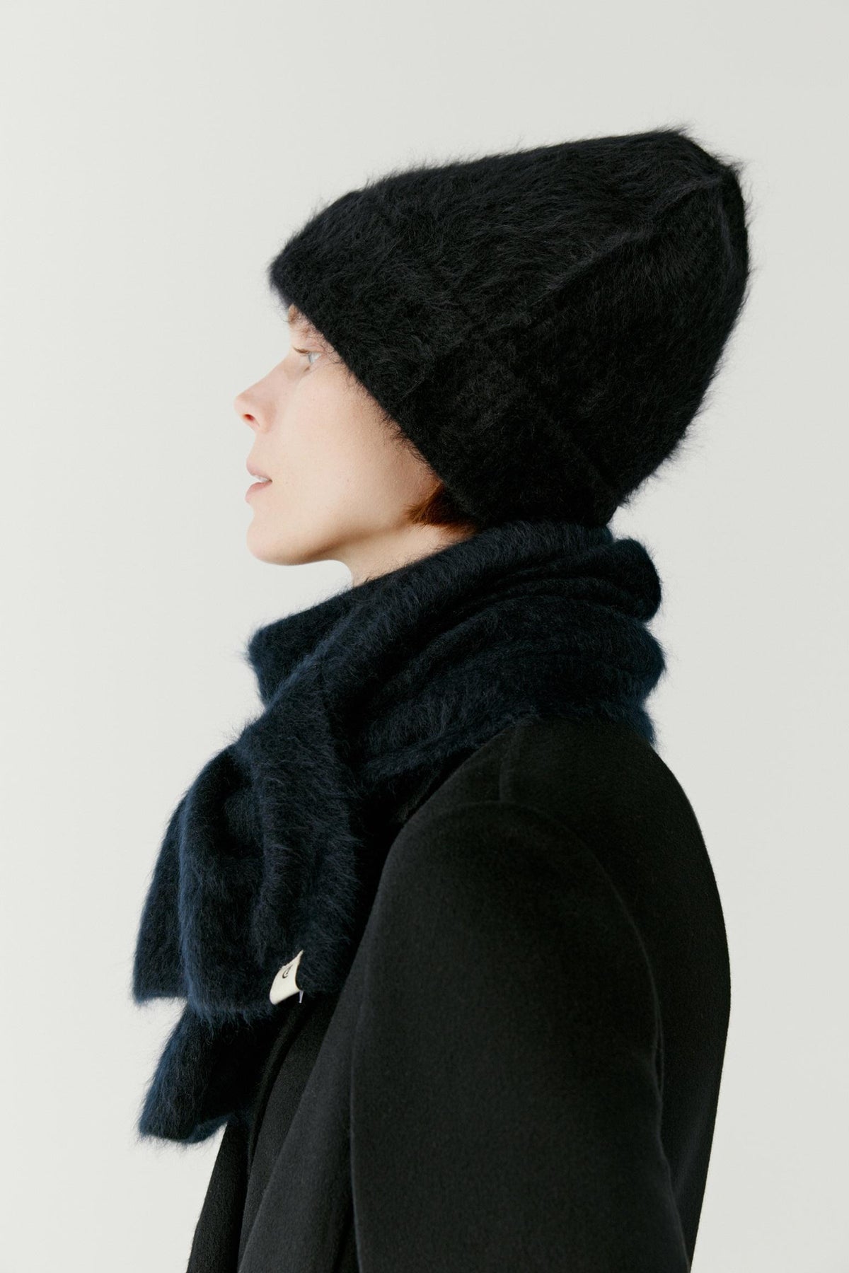 Side view showing the beanie worn as part of a layered winter outfit. The softly structured knit conforms naturally to the head, creating a comfortable and enveloping fit while maintaining a clean, rounded silhouette. The lightweight cashmere texture adds visible softness and volume.