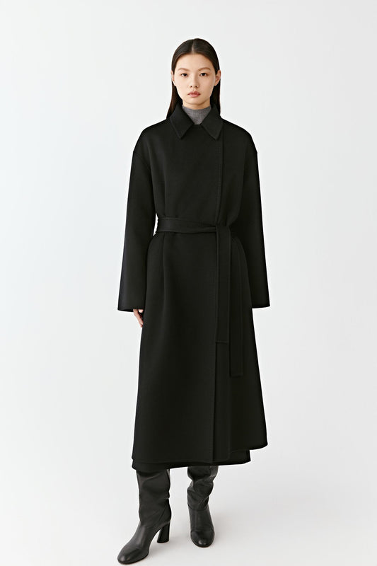 Woman wearing a long black wool coat with a belted waist on a light background