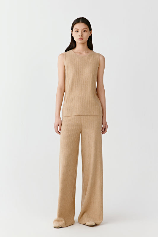 Woman wearing a camel fine ribbed cashmere tank top with a fitted, sleeveless cut, paired with matching trousers; full-length front view highlighting the vertical ribbed texture, clean neckline and close fit through the body.