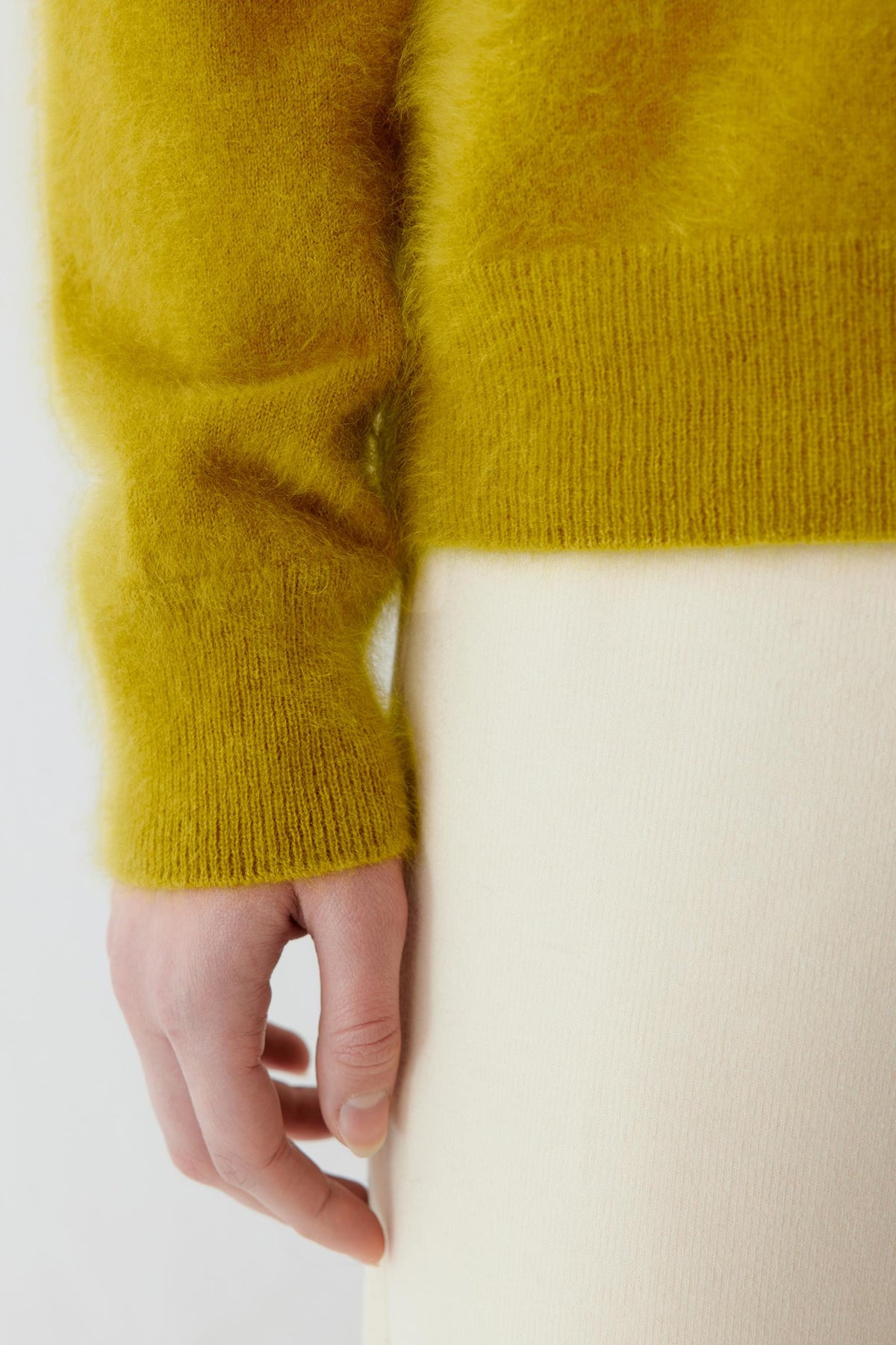 Close-up highlighting the ribbed cuff and fine-knit texture of the mustard yellow cashmere pullover.