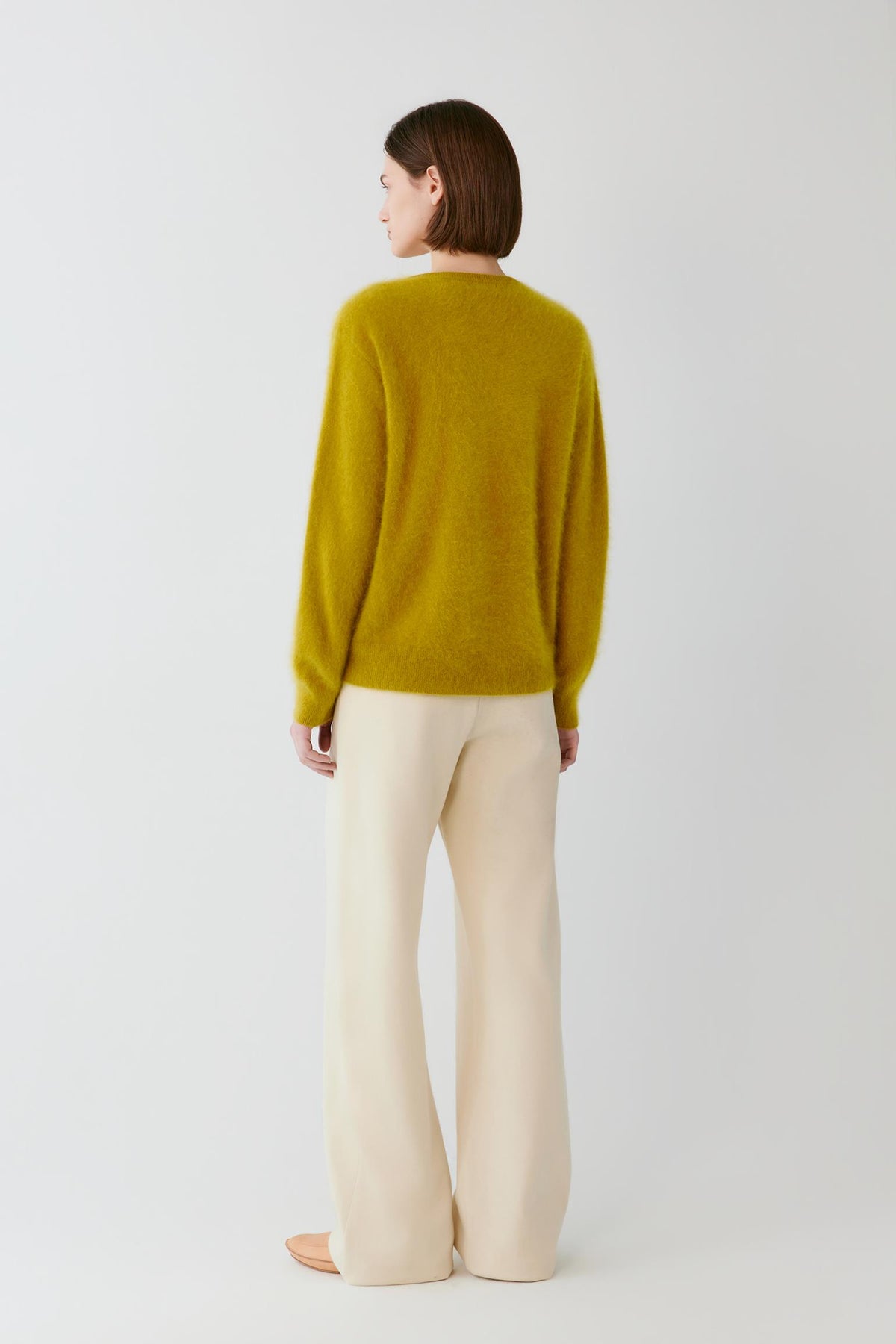 Back view of a woman wearing the mustard yellow cashmere pullover, showing the straight silhouette and long sleeves.