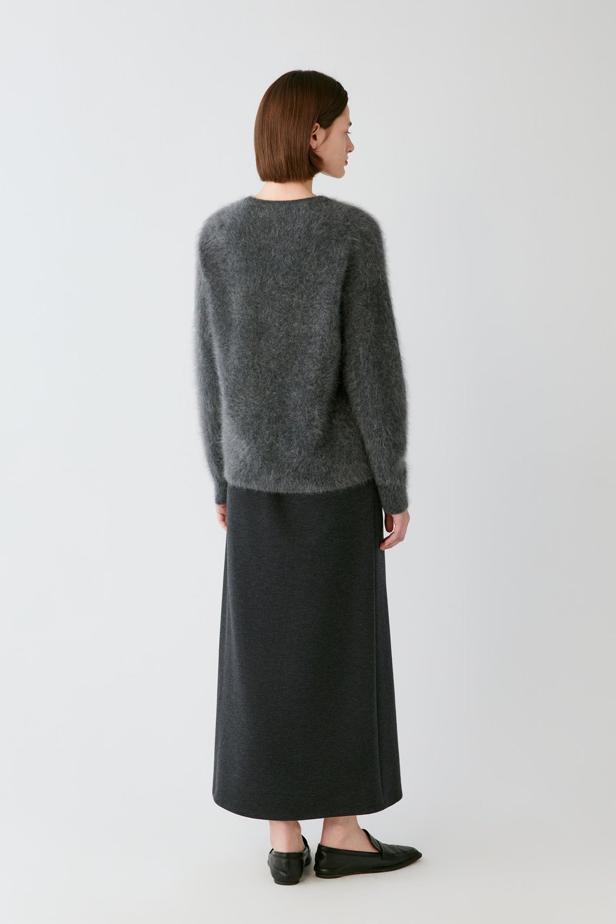 Back full-length view of a woman wearing the smoky grey cashmere pullover, showing the straight silhouette and clean knit construction.
