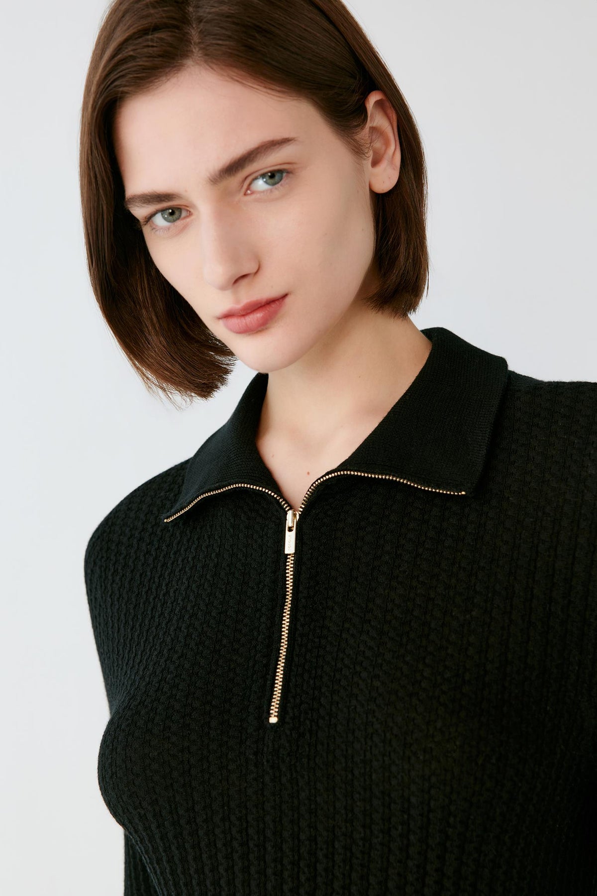 Close-up highlighting the pointed collar, zip neckline and ribbed texture of the deep black worsted wool pullover.