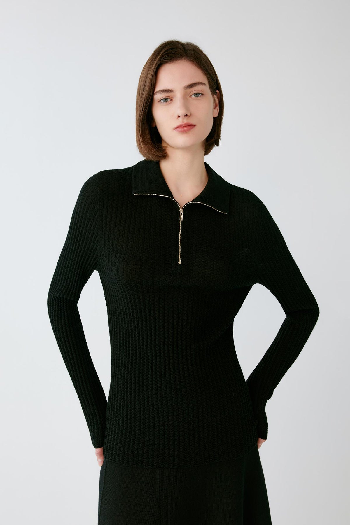 Front view of a woman wearing a deep black worsted wool pullover, showing the zip neckline, pointed collar and fitted silhouette.