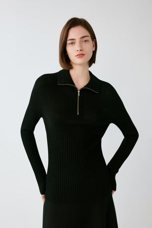 Front view of a woman wearing a deep black worsted wool pullover, showing the zip neckline, pointed collar and fitted silhouette.